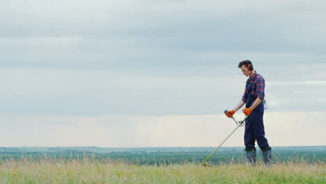 young man mowing grass with a trimmer on a picturesque meadow