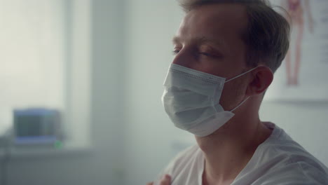 tired patient sitting wearing mask in clinic closeup. man waiting physician.