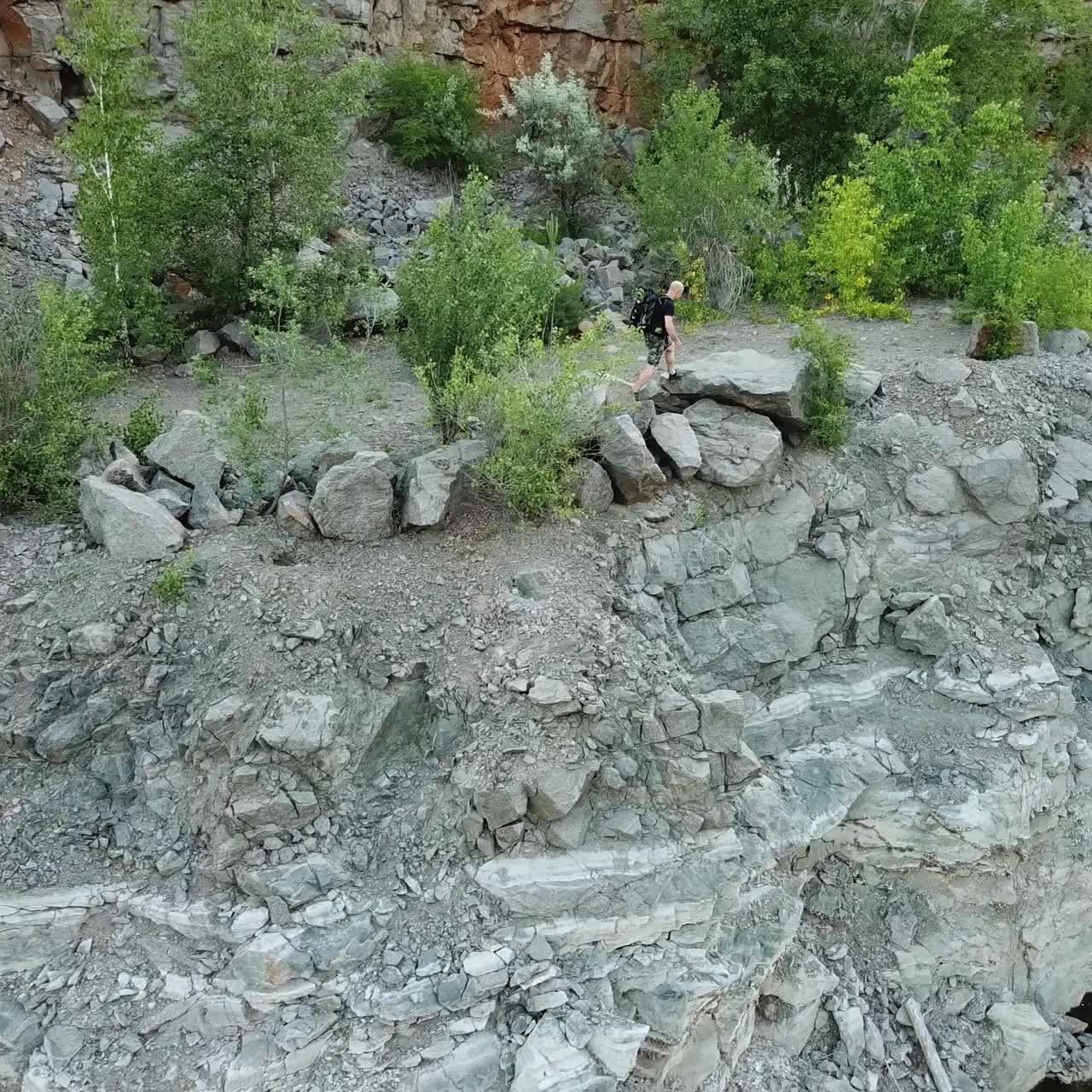 Aerial view of a tourist walks along the rocky shore of a lake. Traveler on the cliff. Camping season