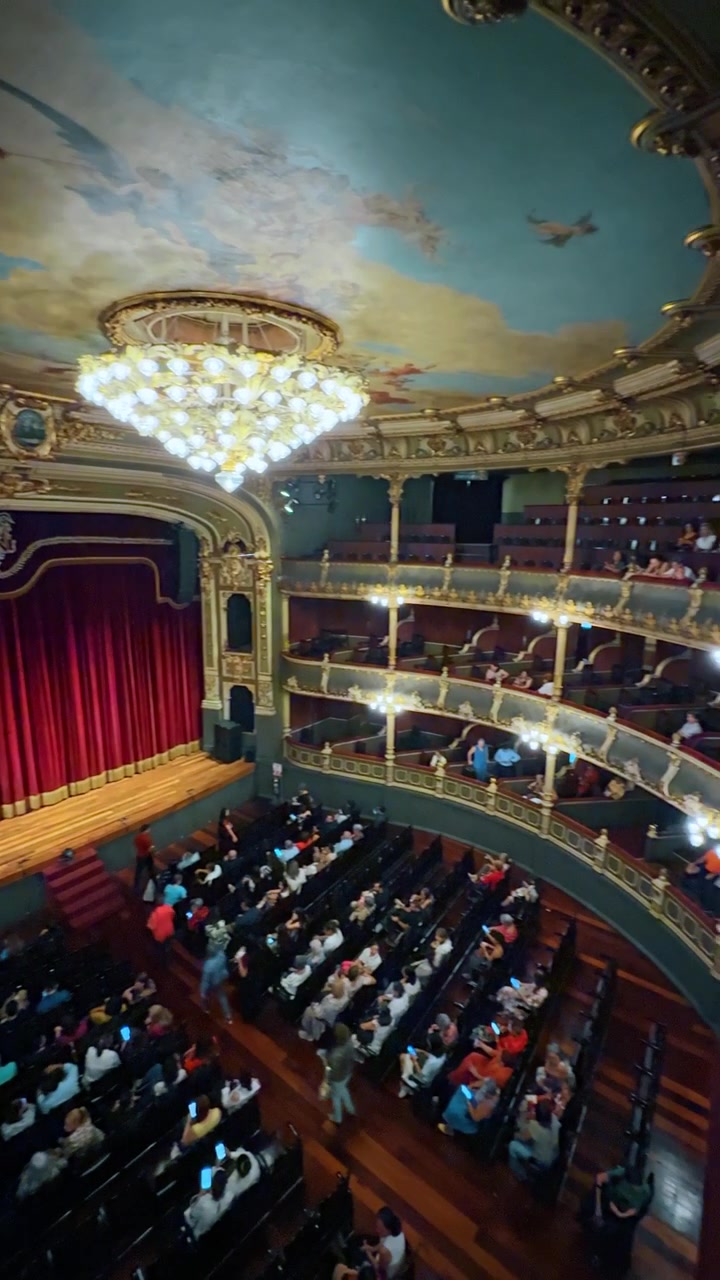 Vista interna del Teatro Nazionale della Costa Rica dal balcone. Sala teatrale storica con sipario rosso e soffitto affrescato.
