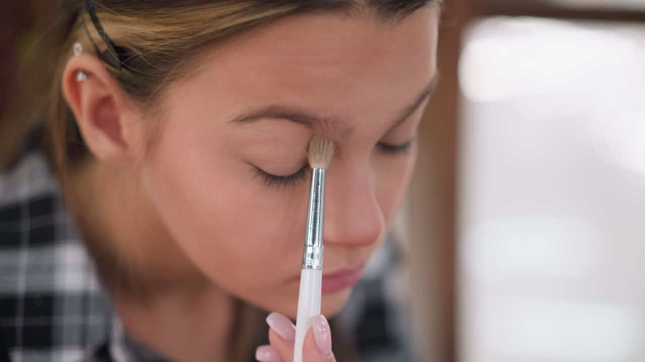 vista de cerca de una mujer que se maquilla con un pincel en el ojo y la frente, aplica cuidadosamente polvo para lograr un aspecto suave e impecable, mejorando su rutina de belleza para un acabado natural