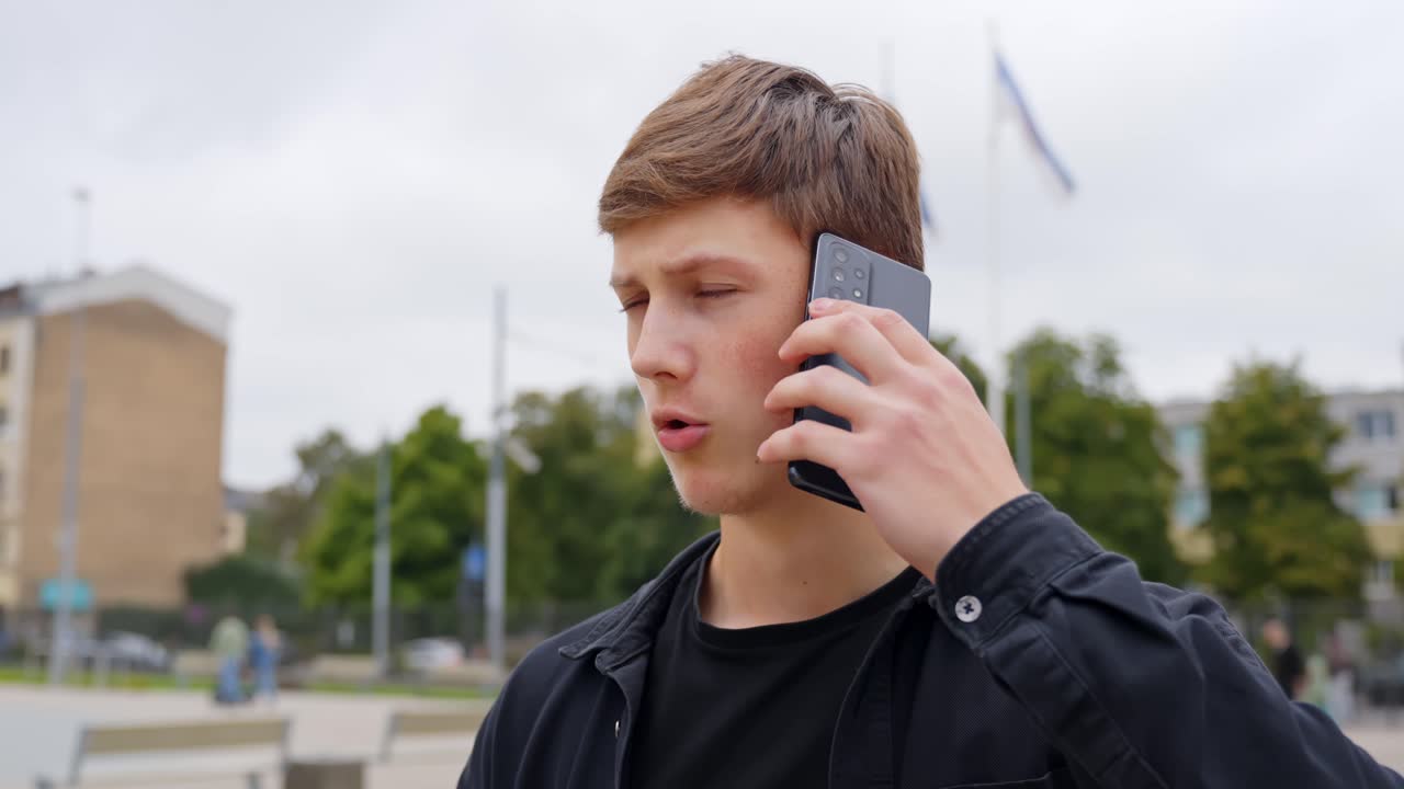 A young man picks up a phone call, reacting with a surprised facial expression to sudden news
