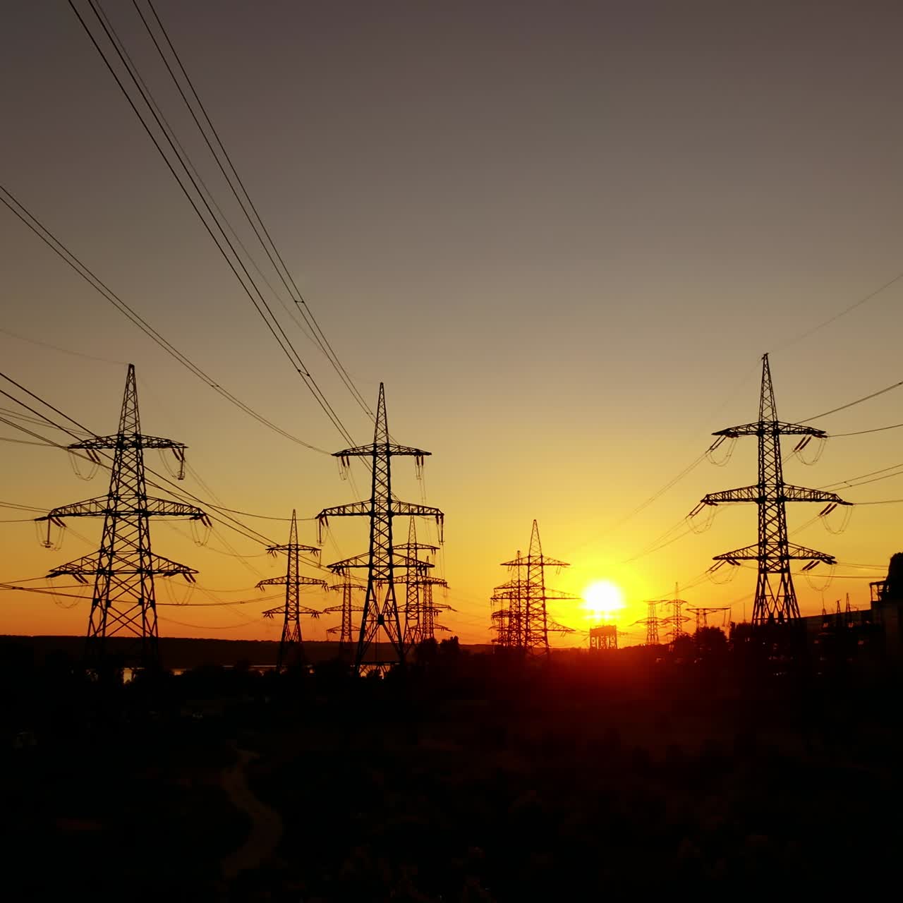 Voltage high electric lines at sunset. Electricity pylons at dusk against orange sun. Silhouette of steel electric towers in the evening.