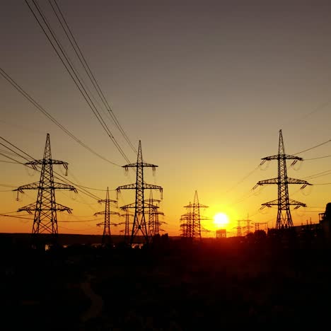 voltage high electric lines at sunset. electricity pylons at dusk against orange sun. silhouette of steel electric towers in the evening.