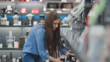 Young-beautiful-girl-in-blue-shirt-chooses-blender-in-appliances-store