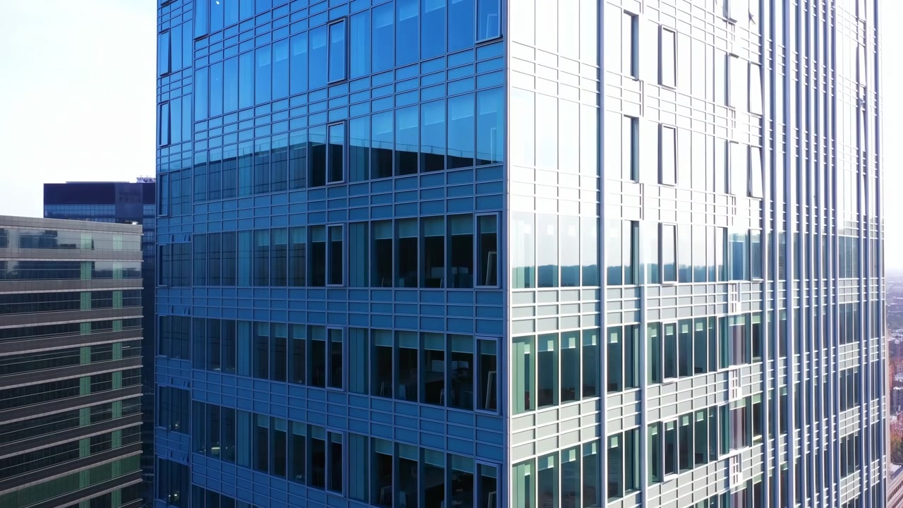 Vista aérea de una moderna torre de oficinas de cristal mostrando la esquina de la sede corporativa con fachada azul reflectante