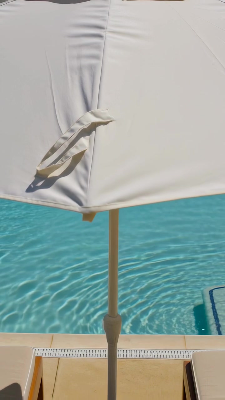 Vertical video: Camera pulling back, revealing large white umbrella at pool showing seam and strap