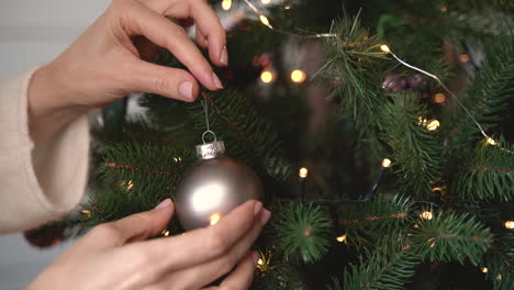 vista de cerca de la mano de la mujer colgando una bola de plata en el árbol de navidad