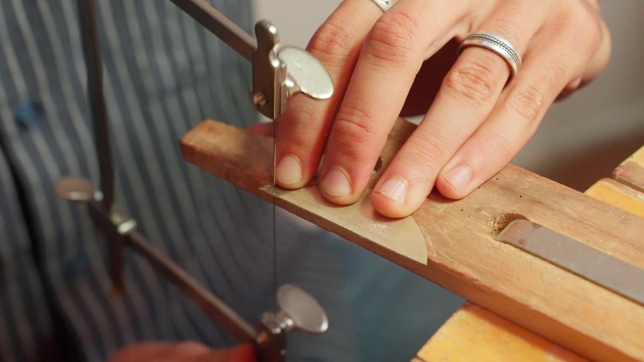 A person saws a piece of wood precisely in a workshop filled with tools and materials.