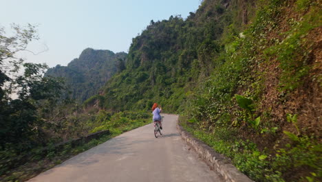woman exploring viet hai village by cycling through the mountains in cat ba island, vietnam. - following shot