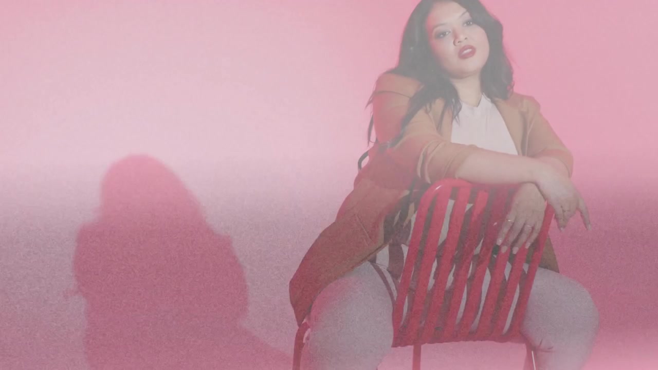 Donna seduta all'indietro su una sedia rossa, con la telecamera che si sposta verso l'alto, una foschia rosa che le oscura il viso per la moda.