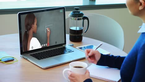 Caucasian-female-student-using-laptop-on-video-call-with-female-teacher,-making-notes