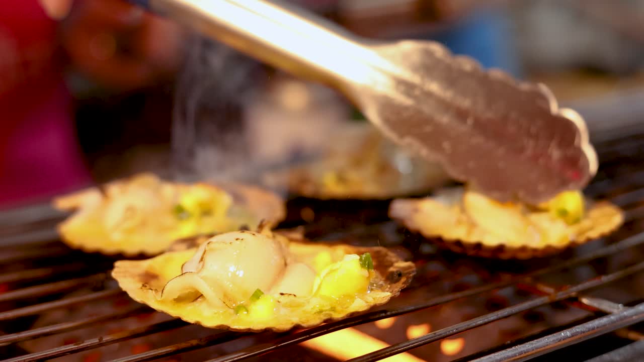 Scallops grilled on open flame, handled with tongs, vibrant street food scene, shallow depth