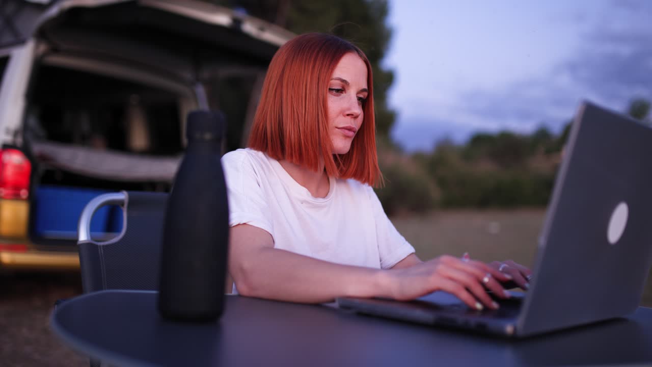Digital Nomad Woman Working on Laptop by Camper Van at Dusk