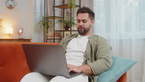 confident young man on sofa couch using laptop making an online video conference call in distance