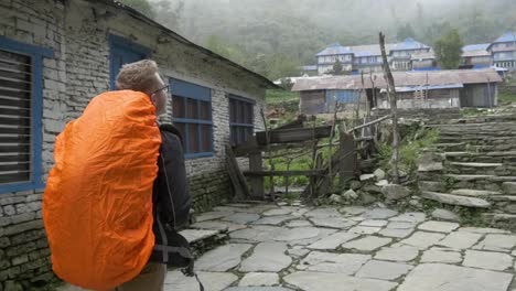 slow motion young man hiking through village in nepal with an orange backpack