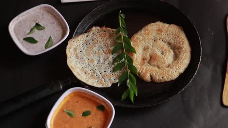 rotating south indian food set dosa with curry and chutney on black background