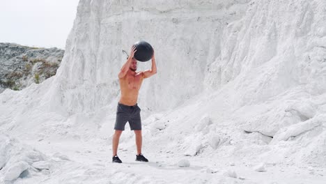 an athletic male strongman does exercises with a fitness ball to strengthen muscles. outdoor activities