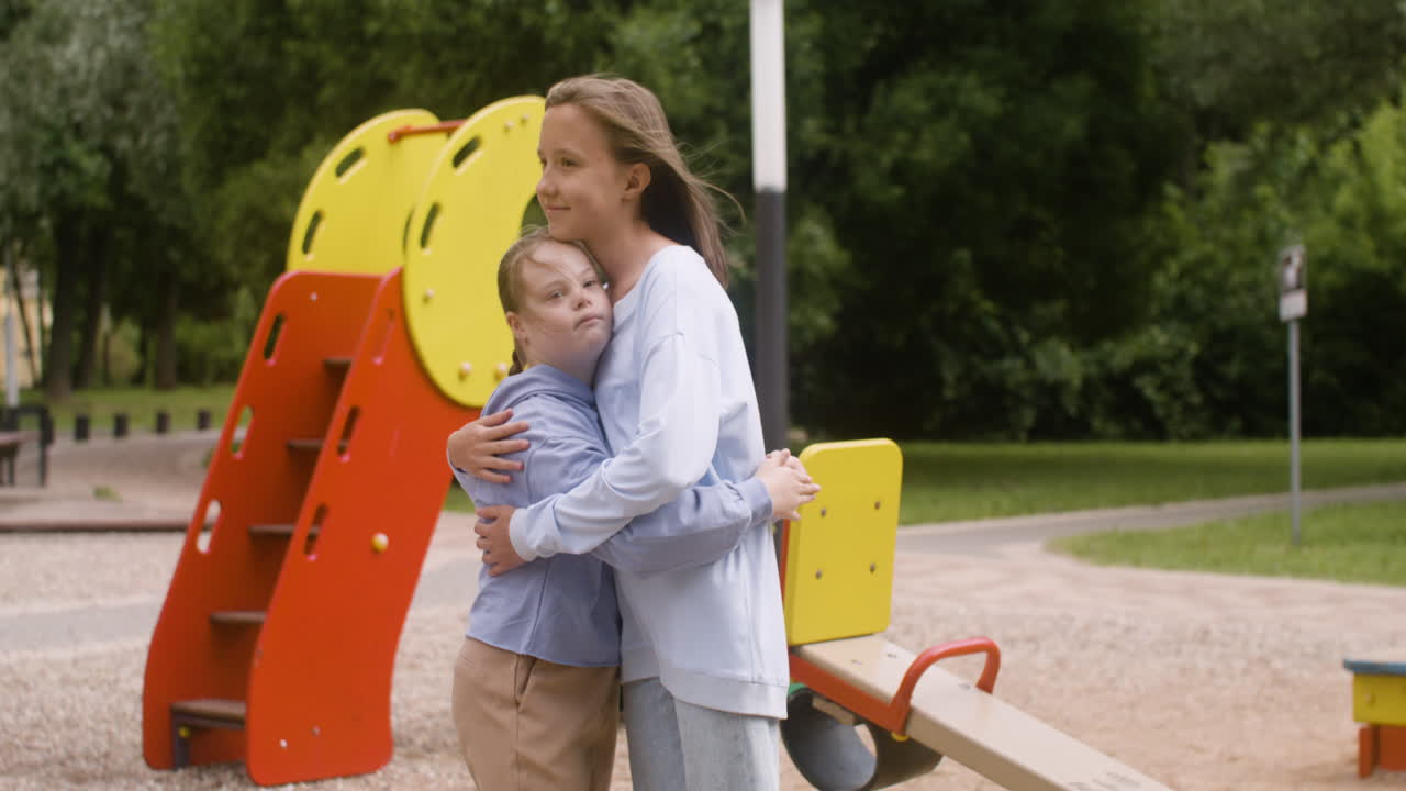 Little girl with down syndrome giving high five and hugging another girl in the park on a windy day