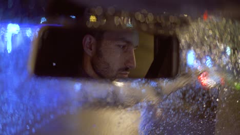 the attractive man sits in the car on the rainy night