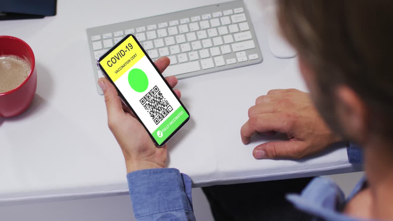 hombre en el escritorio sosteniendo un teléfono inteligente con certificado de vacunación contra la covid y código qr en la pantalla