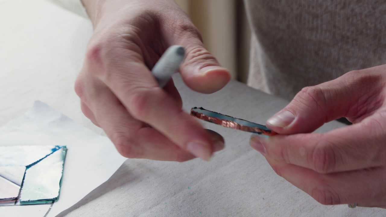 Il nastro di rame viene modellato su un pezzo di vetro tagliato usando il retro di un pennarello durante una lezione d'arte.