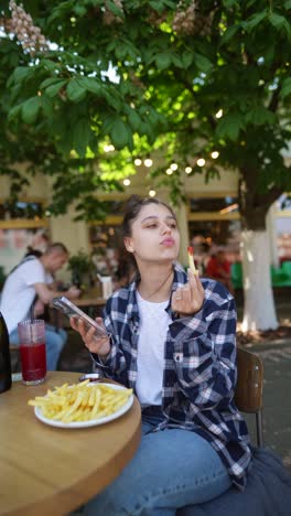 mujer comiendo papas fritas y usando un teléfono inteligente en un café