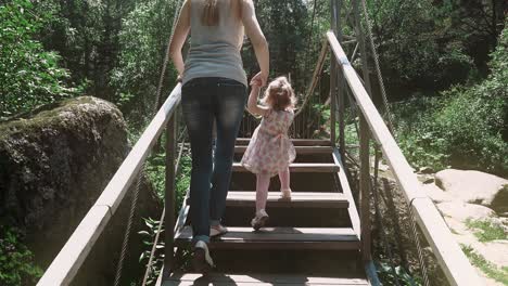 young beautiful mother rises a little child on a wooden bridge across the river in the forest