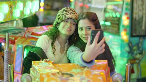 Two friends taking a selfie at a funfair at night