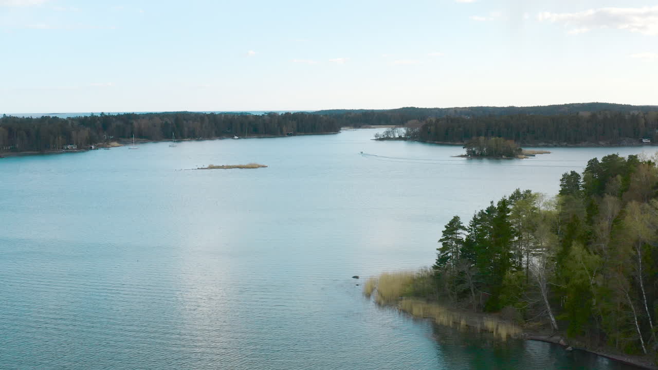 Panning to the left a forested view transition into a the teal blue waters of a Scandinavian lake.