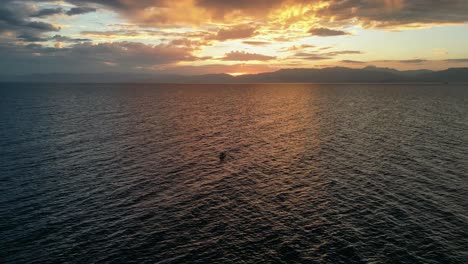 dos personas en canoa hacia la puesta de sol ardiente sobre tierra lejana en el horizonte del océano, disparo de dron