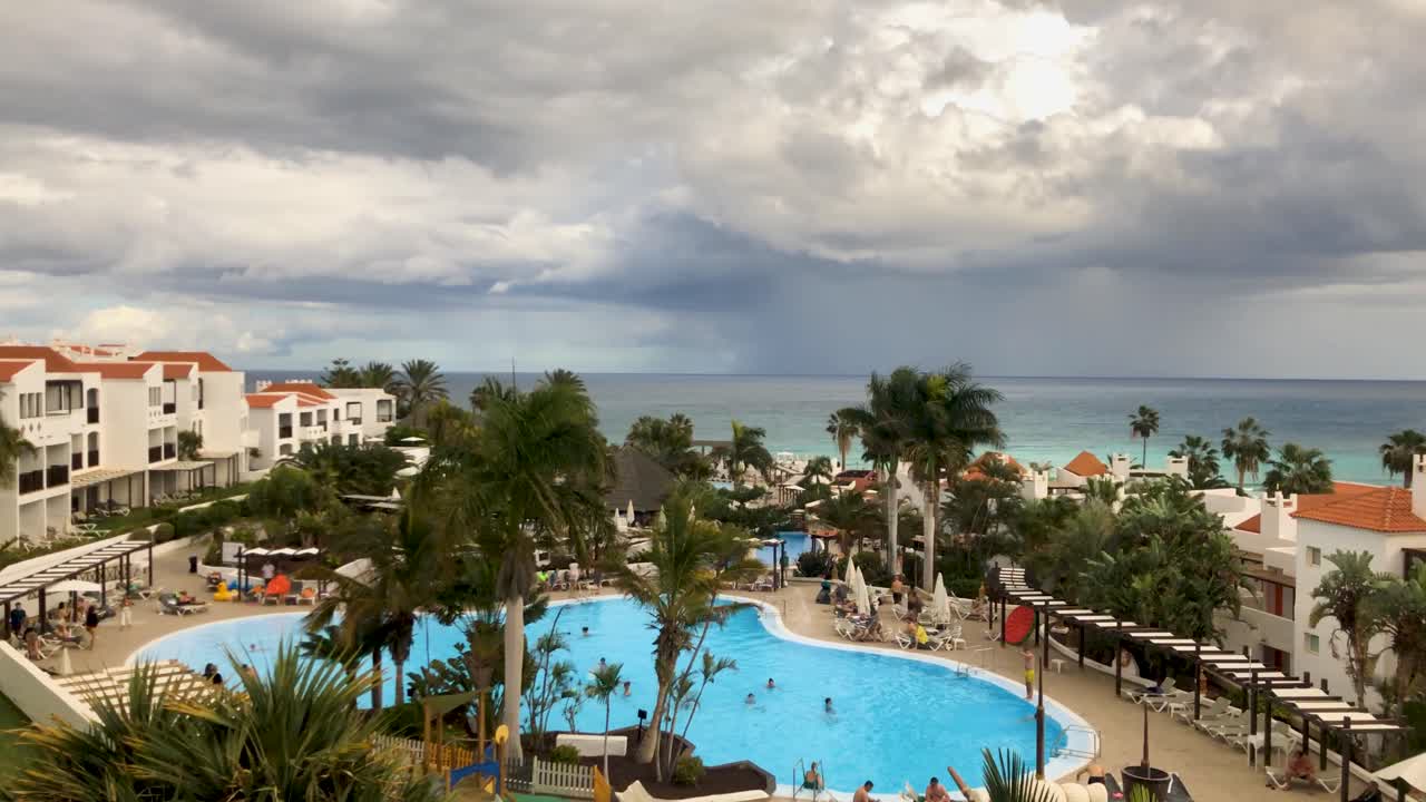 lapso de tiempo panorámico con tormenta de lluvia golpeando un complejo hotelero de lujo en la costa oceánica de la isla canaria