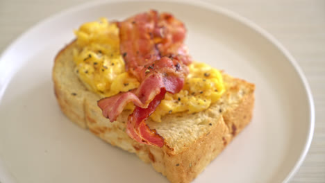 pan tostado con huevos revueltos y tocino en un plato blanco
