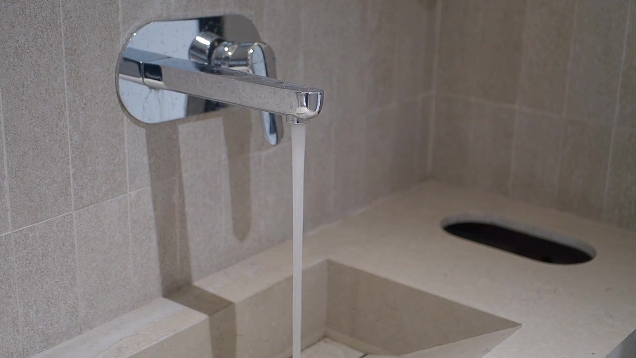 Acqua che scorre da un rubinetto cromato moderno in un lavandino in pietra