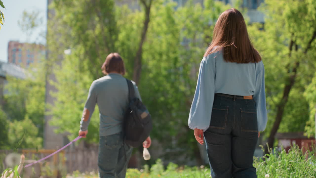 한 커플이 야외를 탐험하며, 두 사람은 키 큰 풀과 멀리 보이는 도시 풍경을 따라 평화롭게 거닐고, 두 명의 사람이 부드러운 빛과 잔잔한 바람이 부는 세련된 초원을 평온하게 산책해요.