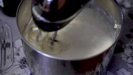 toma superior de la mezcla de crema de claras de huevo batida en un tazón de acero con una batidora en una mesa de madera