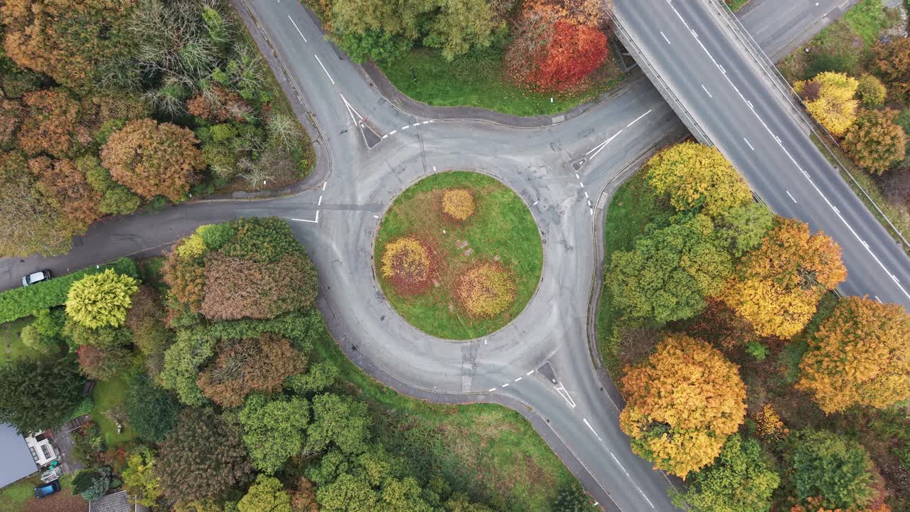 Ascending drone view revealing a traffic roundabout surrounded by colourful autumn trees