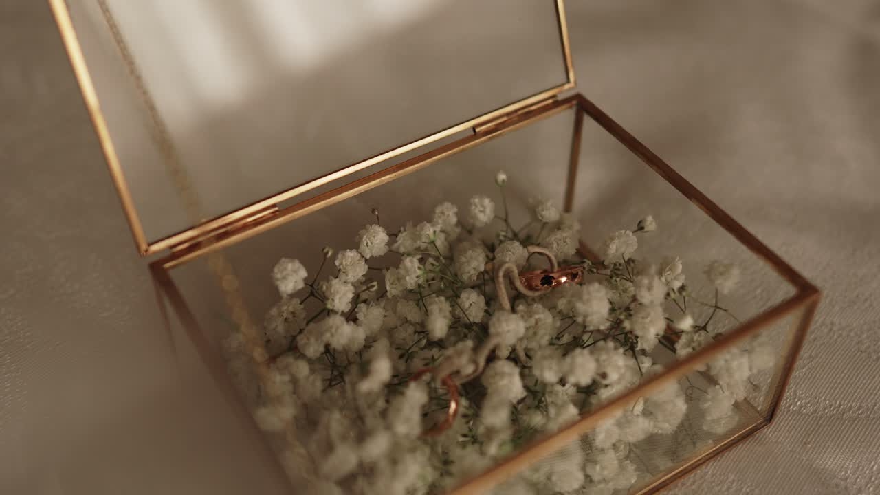 wedding rings rest on white flowers inside transparent glass box