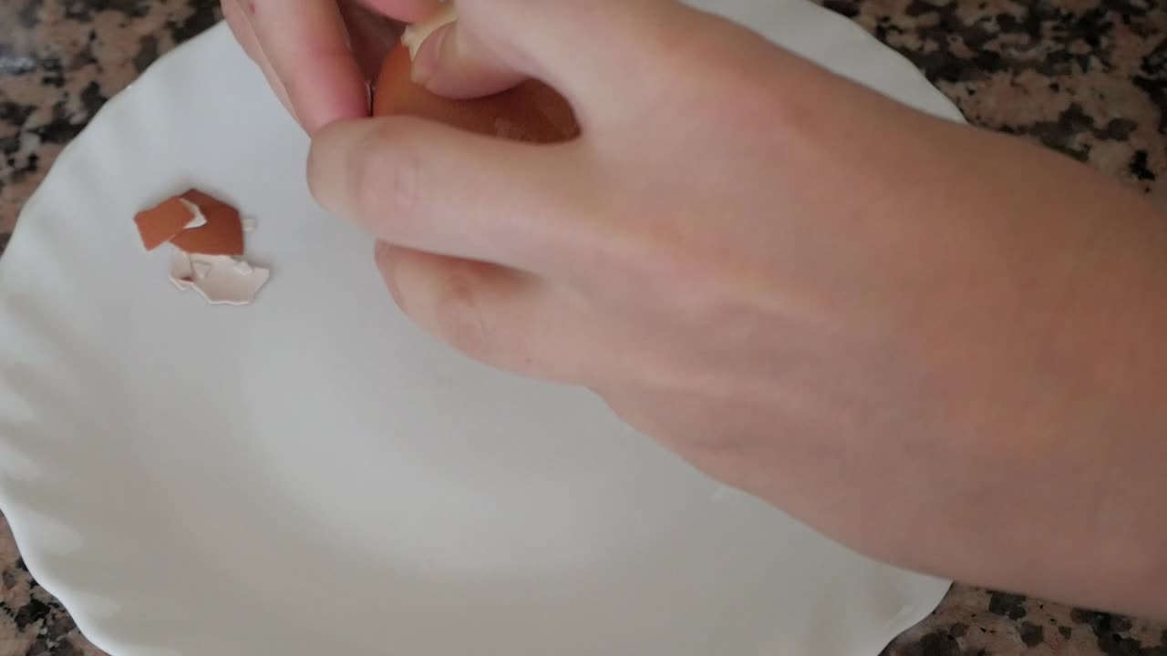 Close-up of woman's hands peeling a hard-boiled egg on a white plate