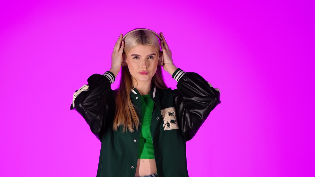 una joven rubia escuchando música con auriculares y bailando, retrato de estudio con fondo rosa