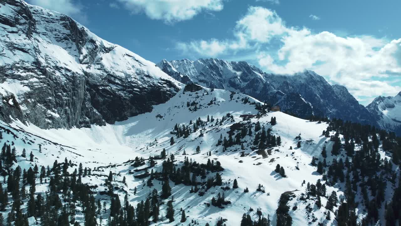 Wide epic alpin mountain panorama flight above scenic Bavaria Elmau castle and snowy glacier peaks in the Bavarian Austrian alps on a cloudy and sunny day along trees, rocks, forest and hills