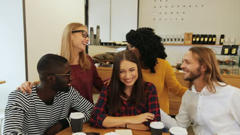 grupo multiétnico de amigos sonriendo y mirando la cámara sentados en una mesa en un café