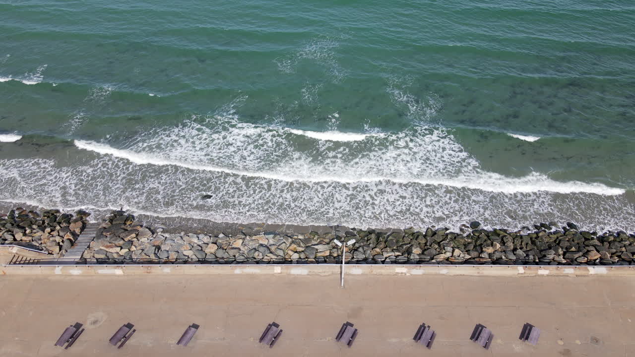 해안의 잔잔한 파도 옆에 산책로를 따라 늘어선 피크닉 테이블의 항공 영상