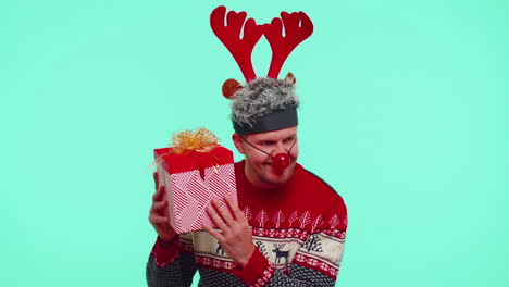 Funny-man-wears-New-Year-sweater-deer-antlers-received-present,-interested-in-what-inside-gift-box