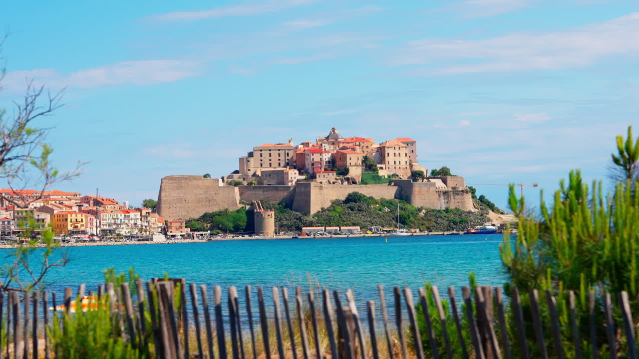 Static shot of the historic town of Calvi in Corsica, France. View of the bastion Citadel overlooking the town. Calm turquoise sea. Summer holidays destination. Mediterranean island