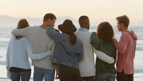 rear view of friends on winter beach watching sunrise together