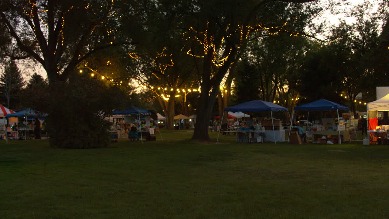 A wide shot of a local business fair and farmers market  in the small city park in the evenings.