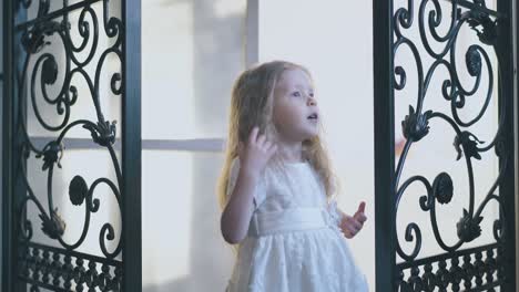 adorable girl in white dances between door forged lattices