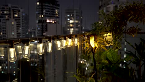 row of dim lit bulbs hanging over balcony railing with flickering light beside plants at night in singapore