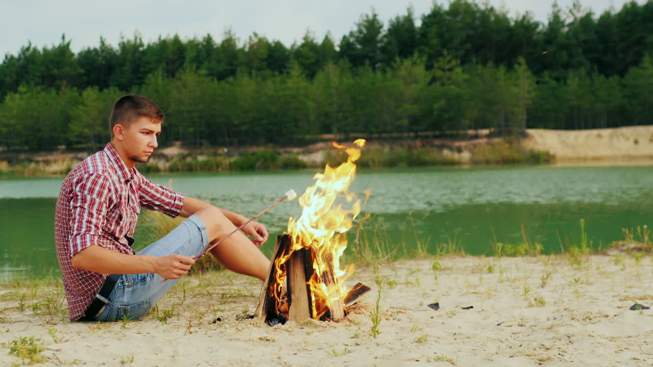 모닥불 옆에 앉아 있는 젊은 매력적인 남자는
